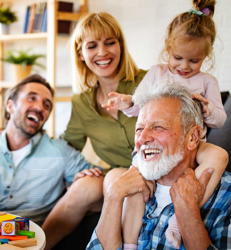 senior-with-family Elderly man laughing with family, including a child on his shoulders, in a cozy living room.