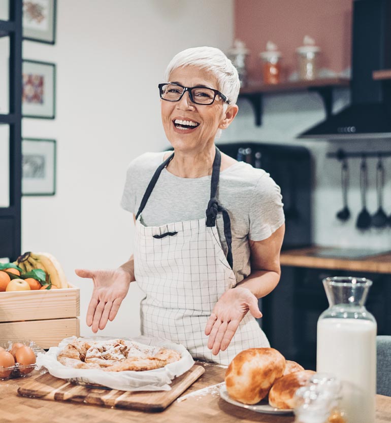 senior-baking Senior woman smiling and presenting freshly baked goods in a modern kitchen at a senior living unit.