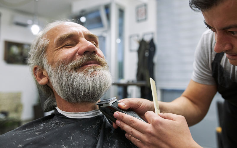 barber-salon Senior man enjoying a beard trim by a barber in a well-lit salon.