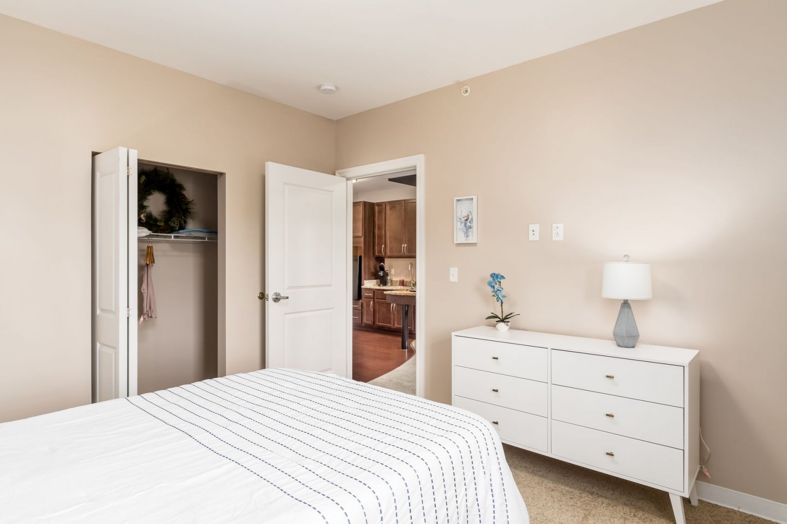 Bedroom with Closet and View into Kitchen Area Bedroom in a living unit featuring a closet, white dresser, and view into a kitchen area.