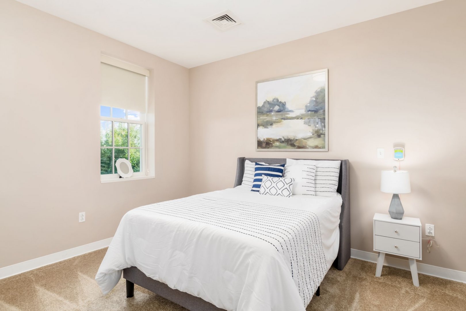 Comfortable and Bright Bedroom Bright bedroom with a large window, bed, side table, lamp, and wall art above the bed.