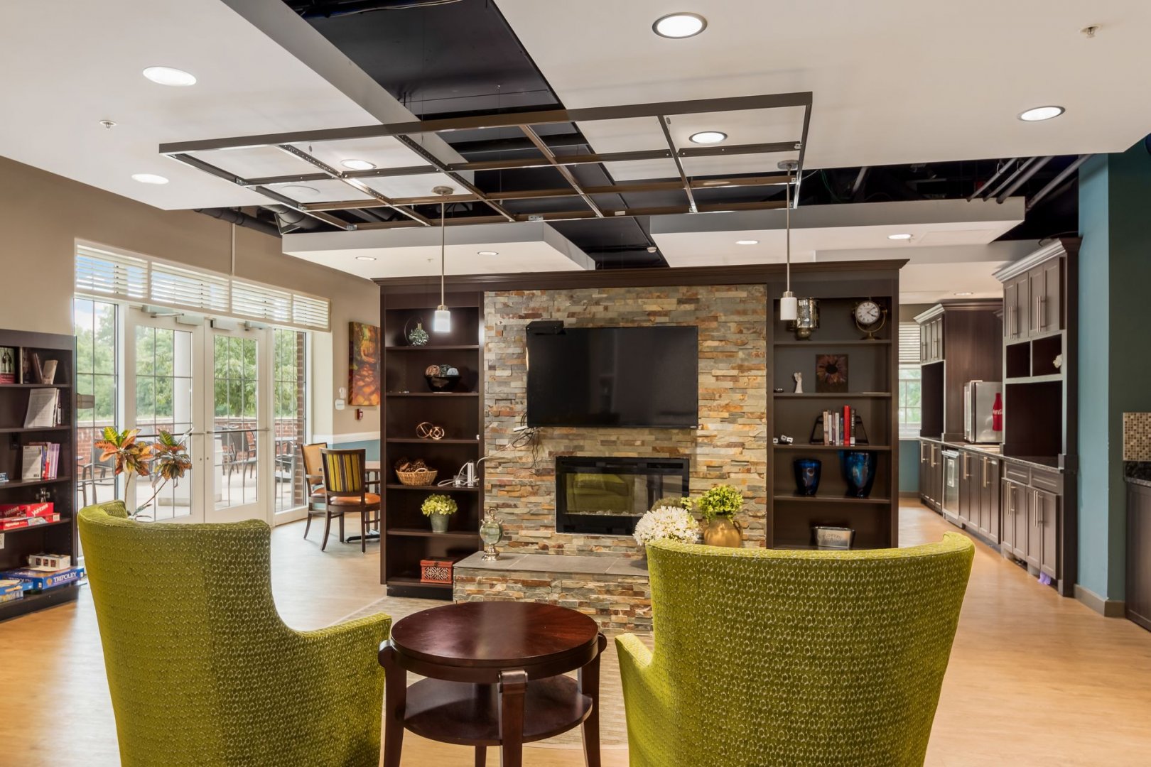 Contemporary Lounge Area in New Albany Senior Living Community Modern lounge area with green chairs, a TV over a stone fireplace, and surrounding bookshelves.