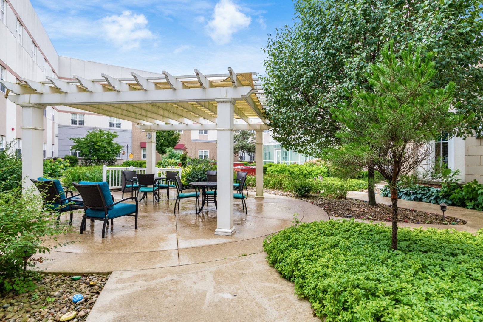 Outdoor Patio Area with Seating and Pergola Outdoor patio area with seating under a pergola surrounded by greenery at a senior living complex.