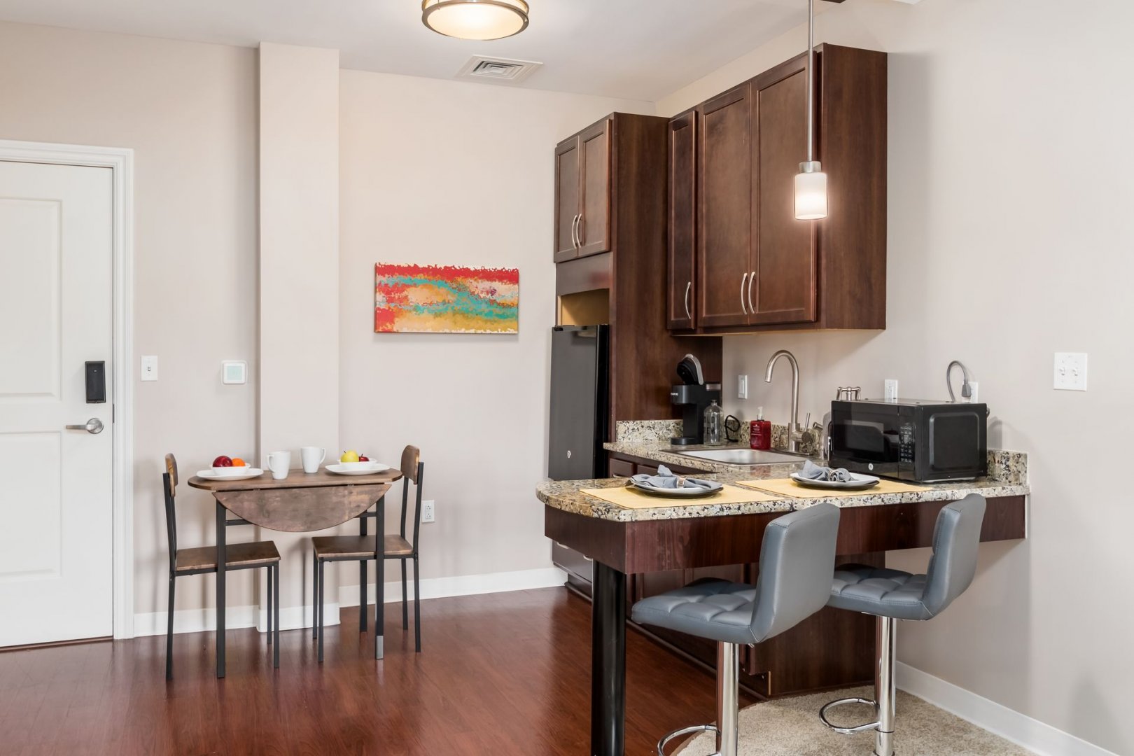 Senior Living Unit Kitchen and Dining Area Modern kitchen and dining area in a senior living unit with wood flooring and painted artwork.